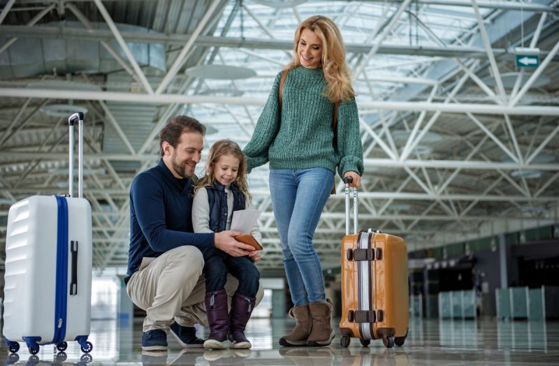 Full length of smiling family with suitcases going abroad. Father and daughter are looking at documents.