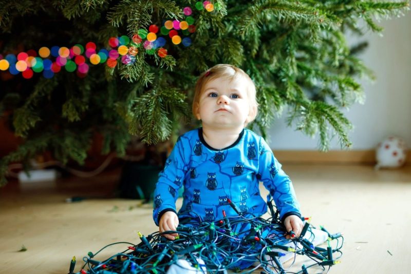 Cute baby girl taking down holiday decorations from Christmas tree. child holding light garland. Family after celebration remove and dispose tree.