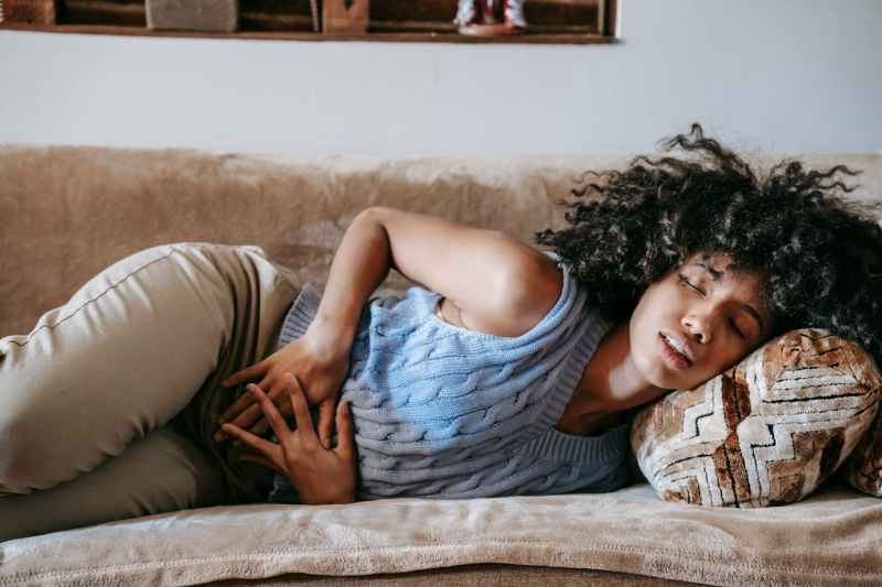 Photo of woman laying on a couch, clutching her stomach in pain due to period cramps.