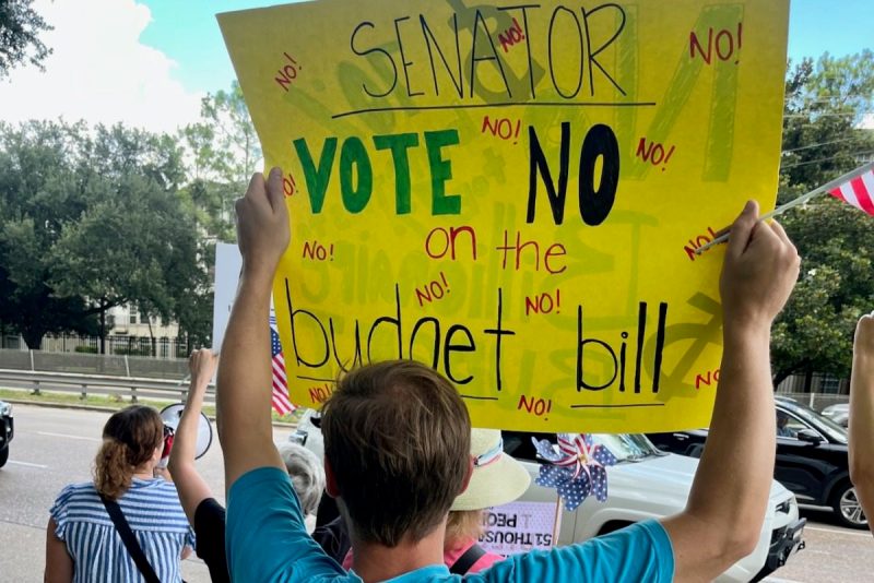 Man holding sign protesting Trump budget bill