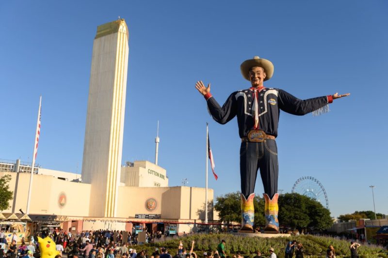 an enormous statue of a cowboy looks over the crowd at the texas state fair