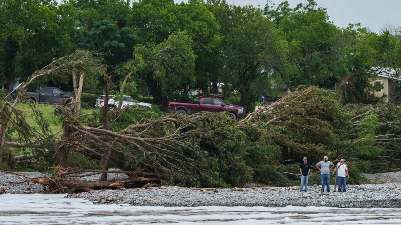 Men stands on the banks of a river surveying flood damage