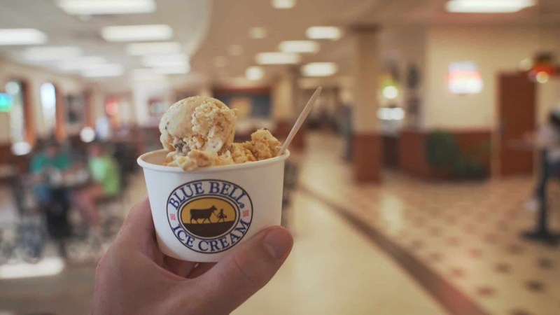 A hand holding Blue Bell Ice Cream in a branded cup