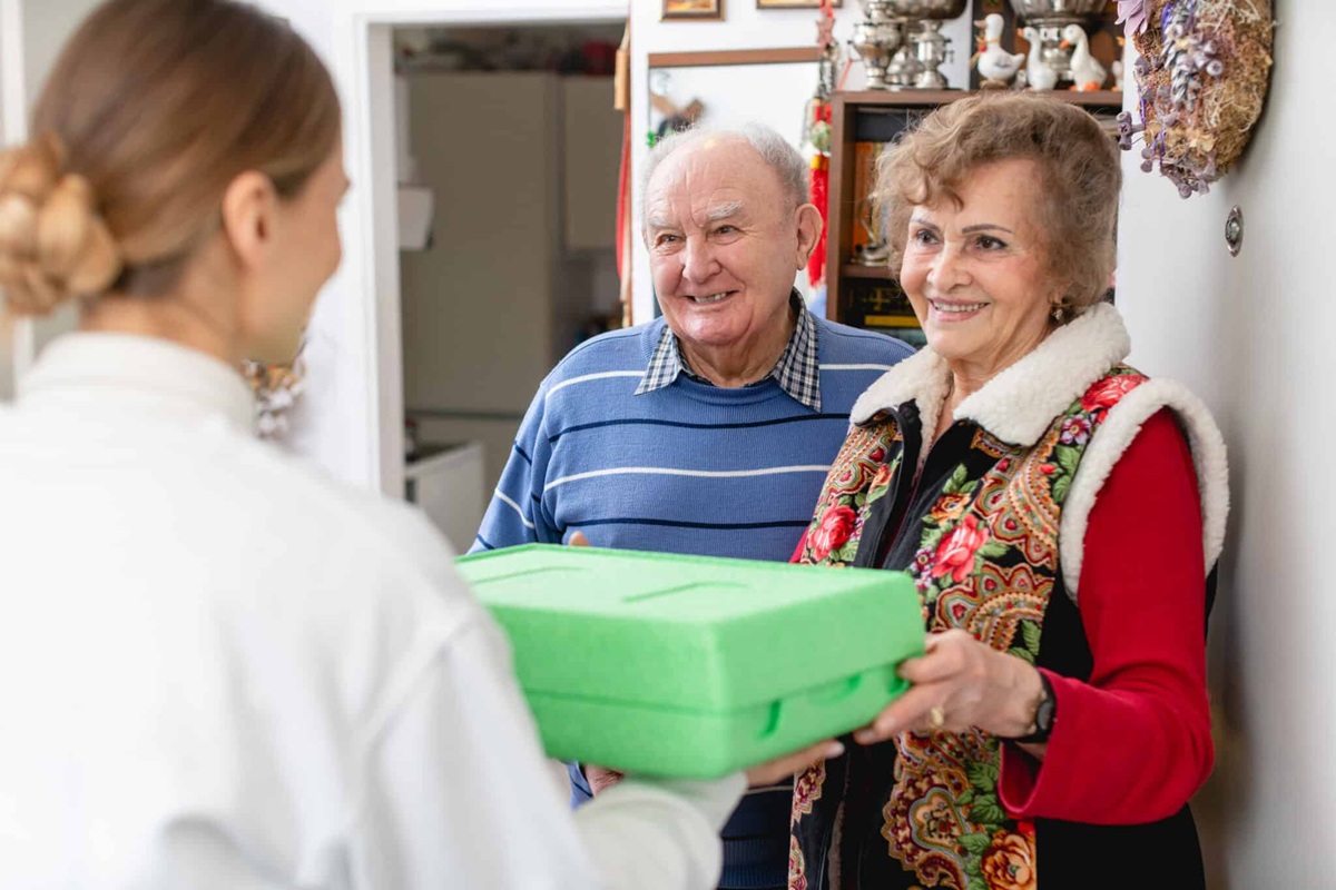 A woman volunteering with Meals on Wheels North Texas drops off food for an elderly couple