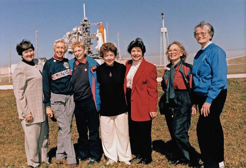 Wally Funk stands with a group of people in front of a space shuttle launch pad