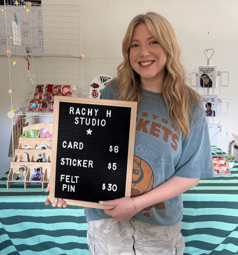 Rachel Klingemann stands with a sign in front of her seller's table.