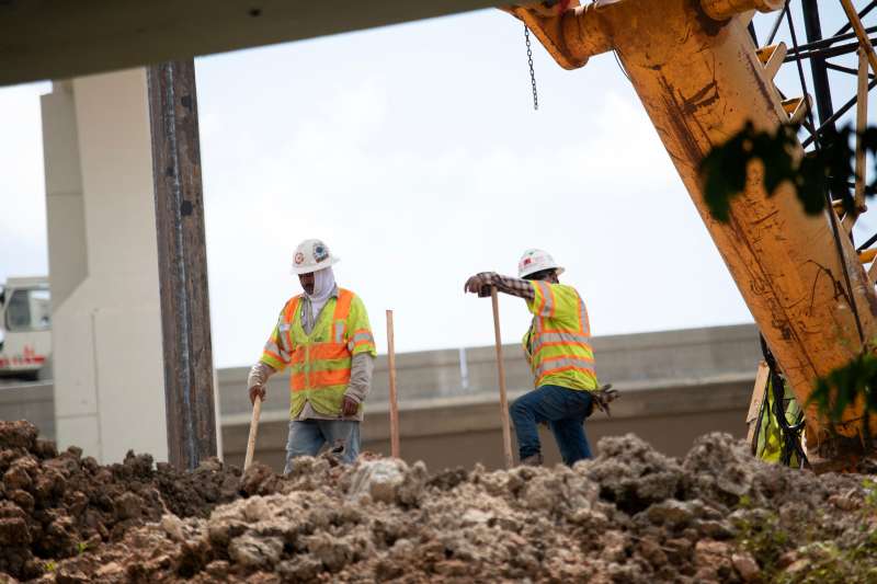 Construction workers under an overpass pause near rubble.