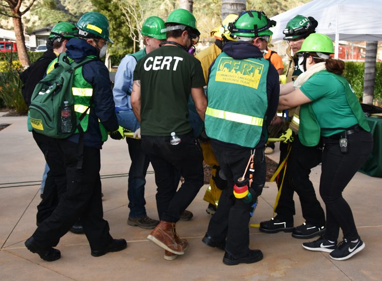 Several people wearing green CERT shirts assisting someone in need.