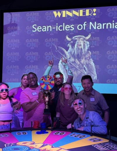 a group of smiling people stand behind a wheel of fortune type wheel