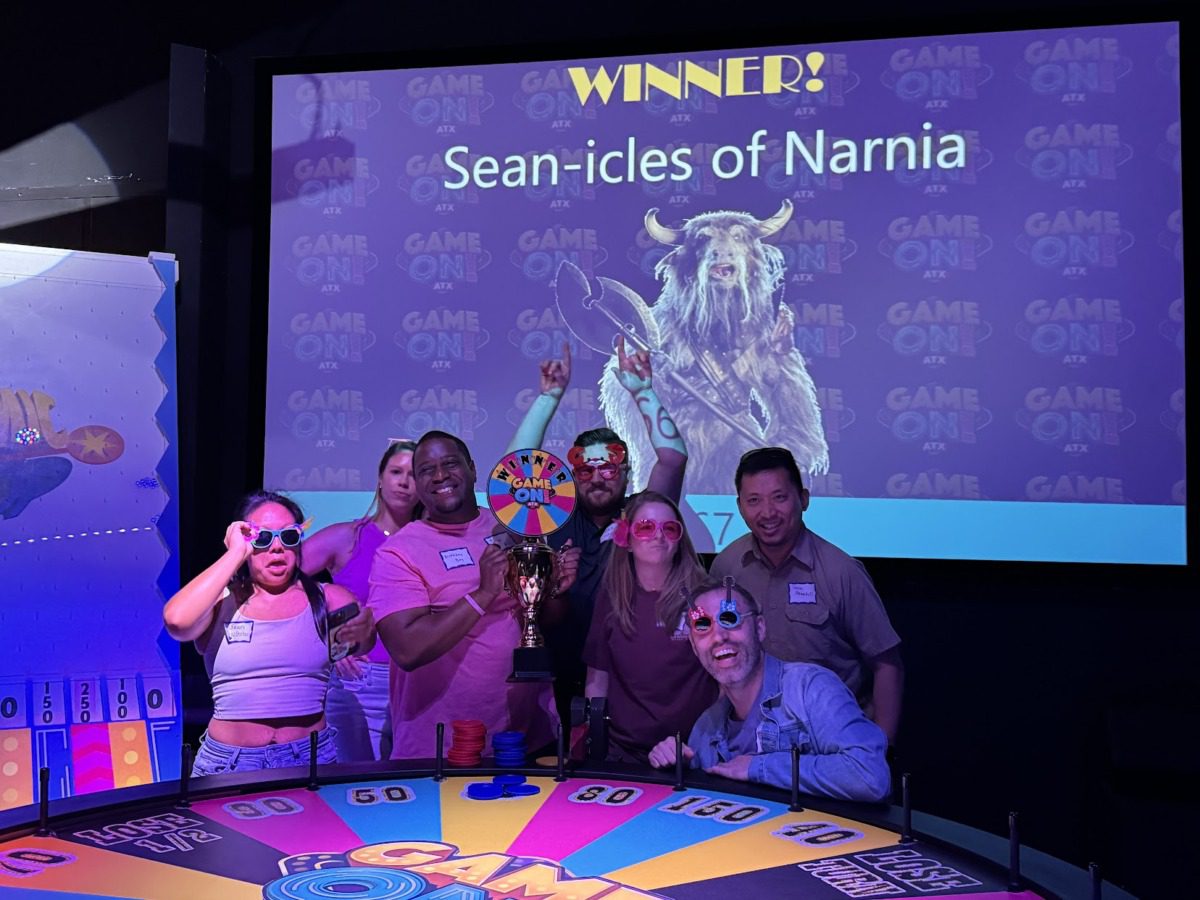 gameon a group of smiling people stand behind a wheel of fortune type wheel